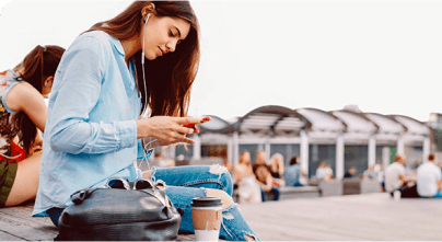 Una joven sentada afuera en un banco jugando con su celular