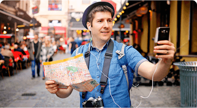 Un turista en la calle de un país extranjero. Sostiene un celular con la mano izquierda y un mapa con la mano derecha.